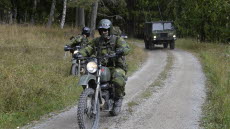 I förgrunden syns två hemvärnssoldater på motorcykel. I bakgrunden syns ett annat militärfordon. 